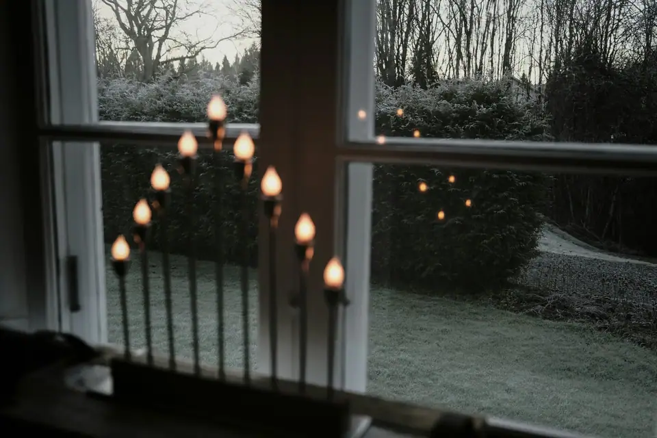An electric candle bridge on a windowsill, looking out over a frosty garden at dusk