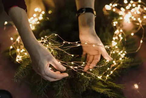 Hands threading fairy lights through a Christmas wreath