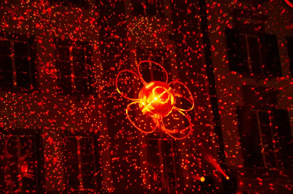Hundreds of red laser dots projected across a building front at night, with a glowing red flower shape in the middle