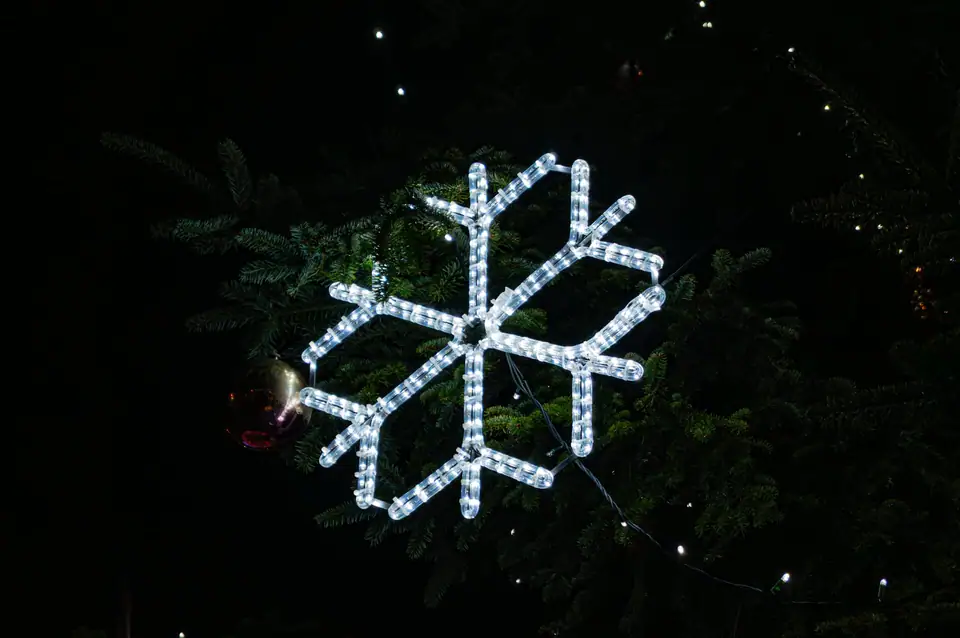 A white LED snowflake light hanging on the branches of a fir tree at night
